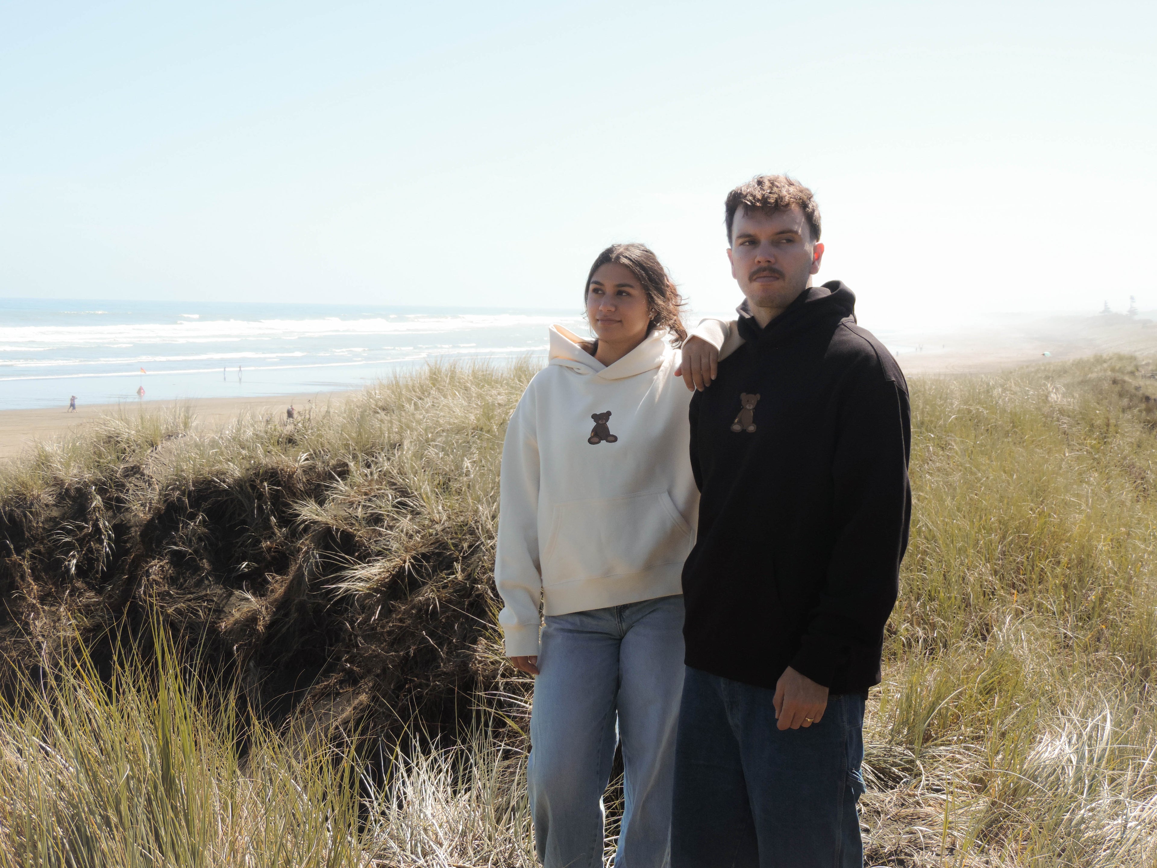 Two people standing on a beach with grassy dunes in the foreground